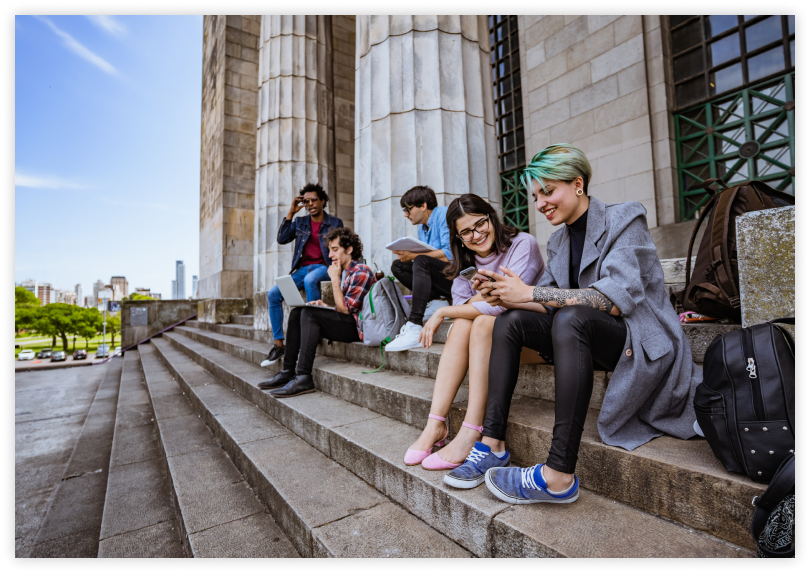Two young adults sit on building steps while looking together at a smartphone.