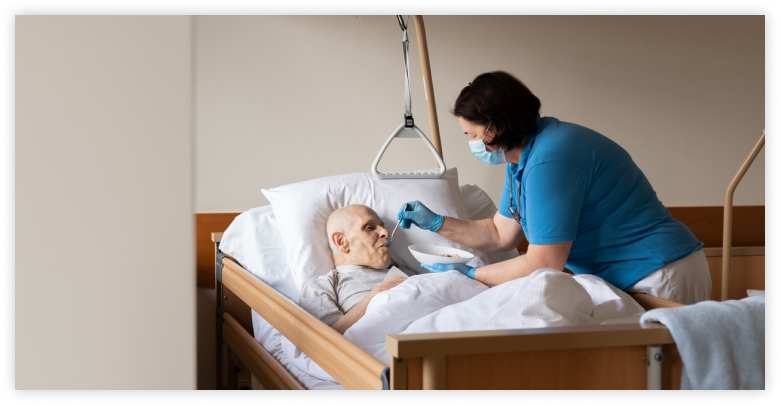 Nurse feeds older man in hospital bed.